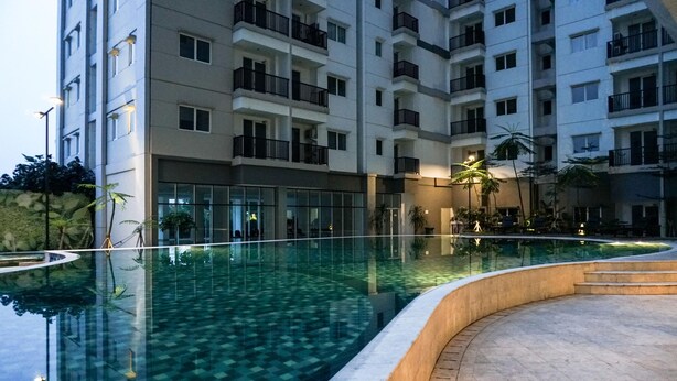 A modern hotel with a large indoor swimming pool, multiple balconies, and a well-lit outdoor area with plants. - Strategic And Comfy Studio Apartment At Signature Park Grande (Jakarta)