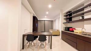 A modern kitchen with dark wooden cabinets, a dining table with two chairs, and a sofa in the background. - Modern And Stylish 2Br (No Kitchen) Apartment At Skales Residence Nusa Dua Bali (Nusa Dua)