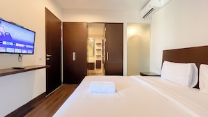 A hotel room with a bed, a TV mounted on the wall, a wooden nightstand, and a wardrobe. - Modern And Stylish 2Br (No Kitchen) Apartment At Skales Residence Nusa Dua Bali (Nusa Dua)