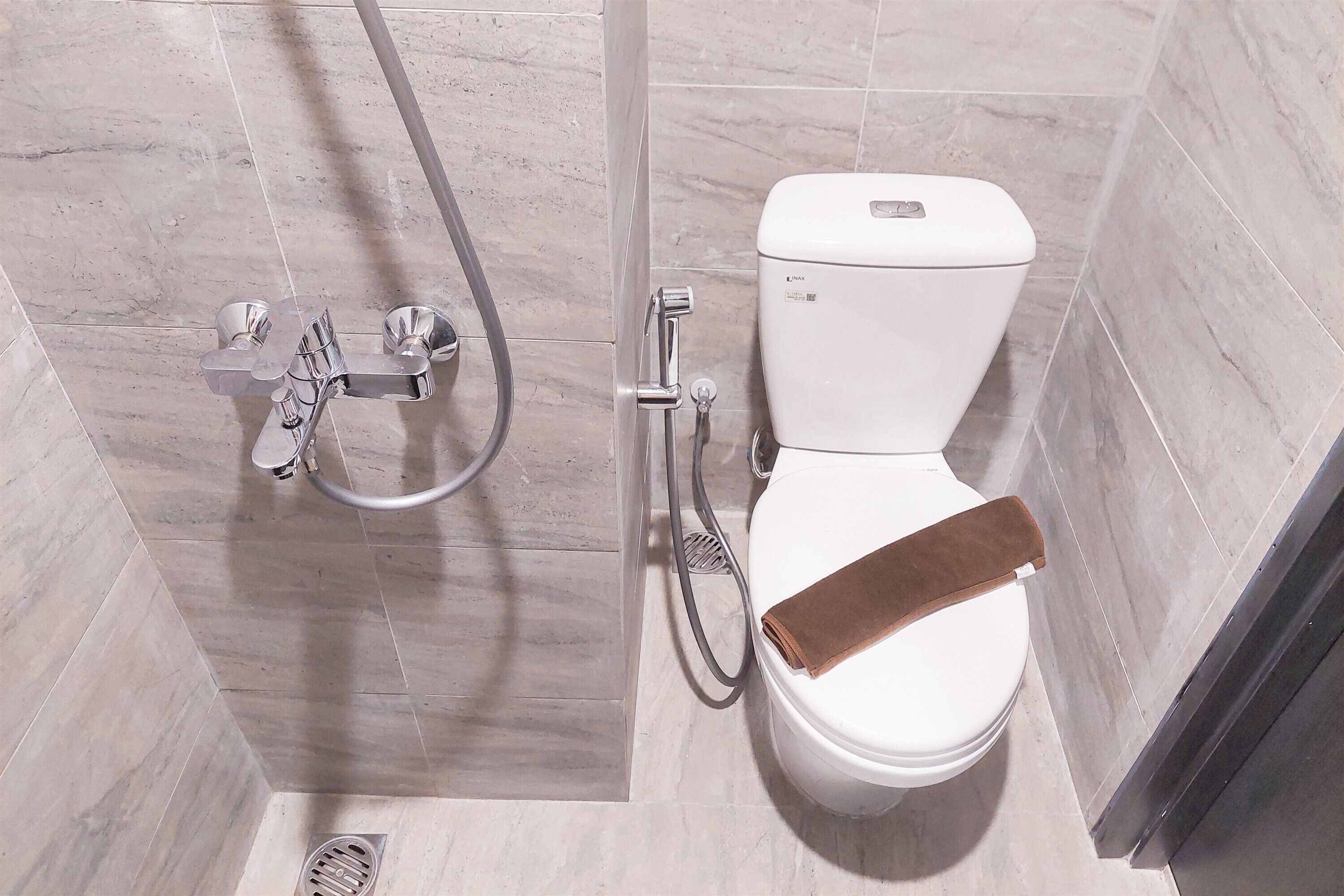 A bathroom with a white toilet, a shower with a handheld showerhead, and a towel rack.