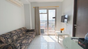 A modern living room with a patterned sofa, a glass table with a vase, and a TV mounted on the wall. - The Elevated Abode 2Br At Mekarwangi Square Cibaduyut Apartment (Bandung)