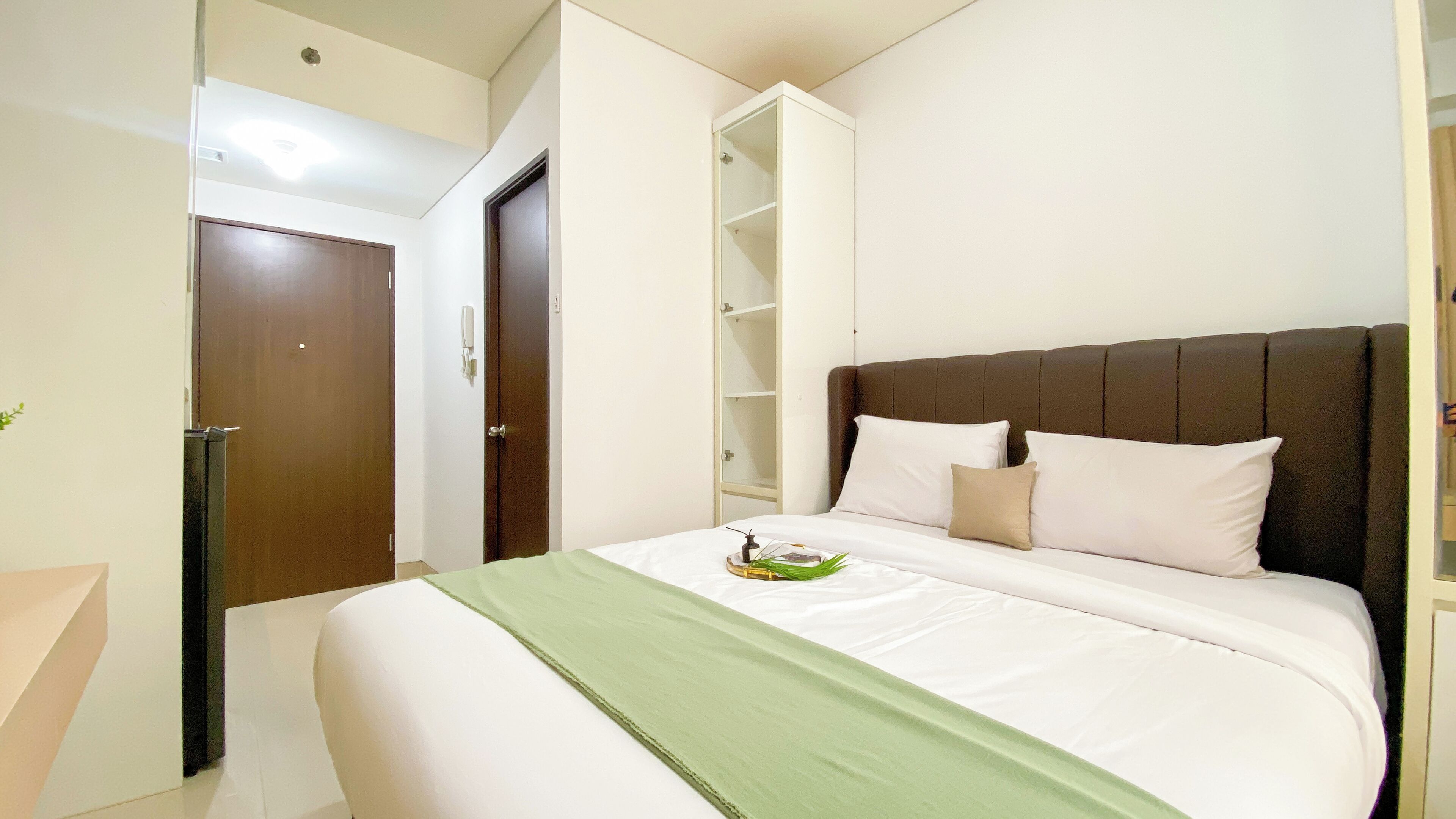 A neatly made bed with a green throw, a brown headboard, and a white bedside table with a small plant.