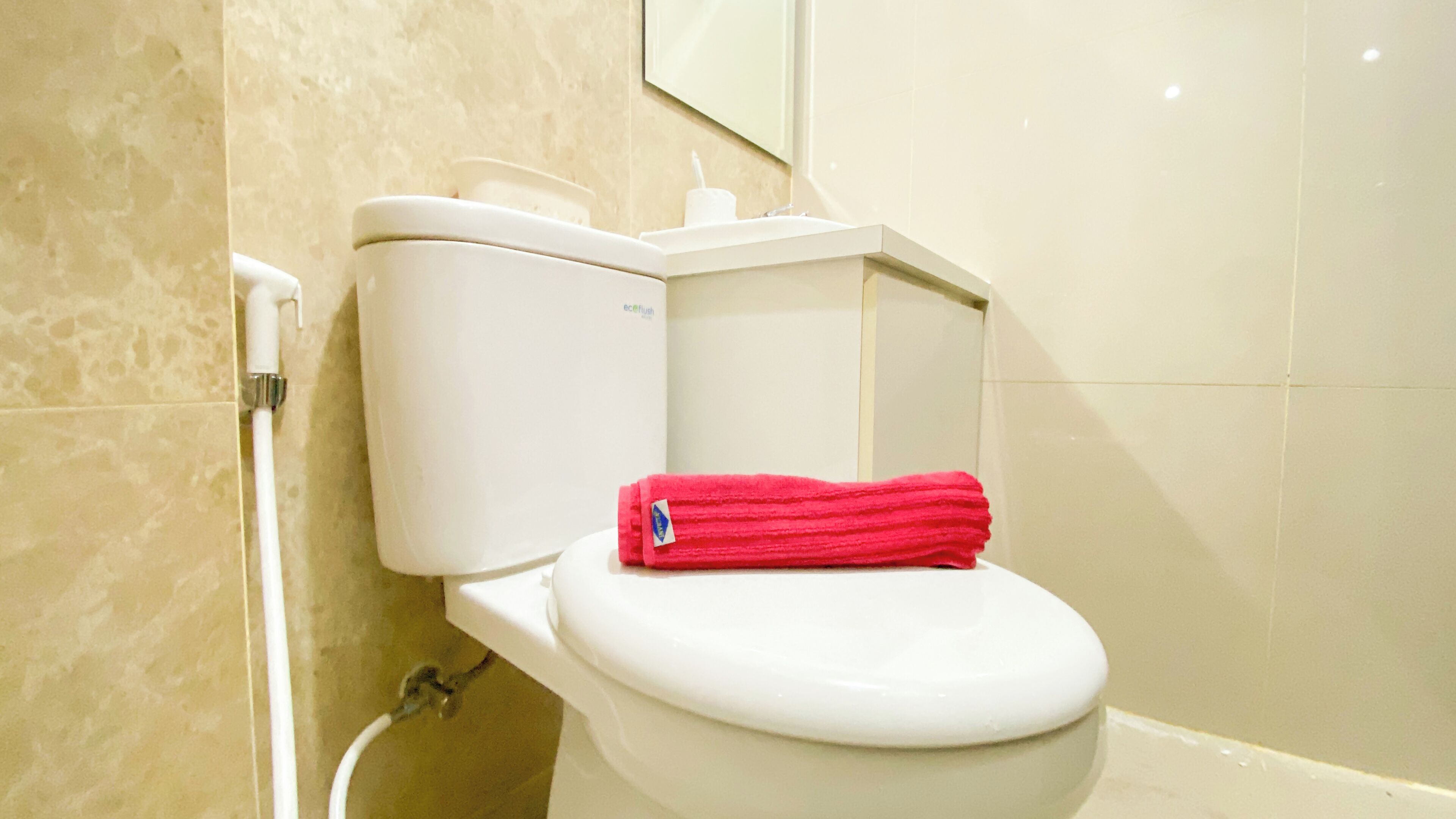 A toilet with a white tank and seat, a red towel on the seat, and a toilet paper holder on the tank.