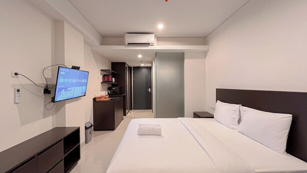 A modern hotel room with a large bed, a flat-screen TV mounted on the wall, a small desk, and a wardrobe. - Stylish Studio (No Kitchen) Apartment At Skales Residence Nusa Dua Bali (Nusa Dua)