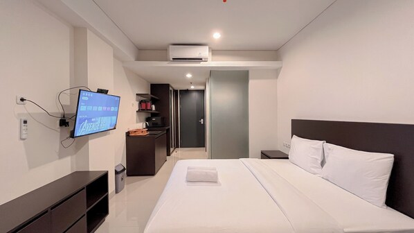 Quarto de hotel moderno com cama grande, televisão de tela plana na parede, escrivaninha pequena e guarda-roupa.