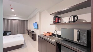 Une chambre d’hôtel comprenant un lit, une télévision, une kitchenette équipée d’un four à micro-ondes, d’une machine à café et d’un panier.