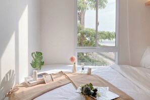 A neatly made bed with a view of greenery outside, a potted plant, a vase with flowers, and a few books on the bed. - Lovely And Comfy 2Br Apartment Tokyo Riverside Pik 2 (Teluknaga)