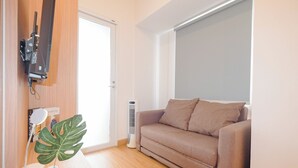 Un salon avec un canapé, un téléviseur fixé au mur, un radiateur et une grande plante.
