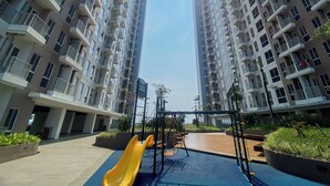 Un terrain de jeux avec un toboggan jaune et des balançoires, situé dans un quartier résidentiel composé d’immeubles à étages élevés.