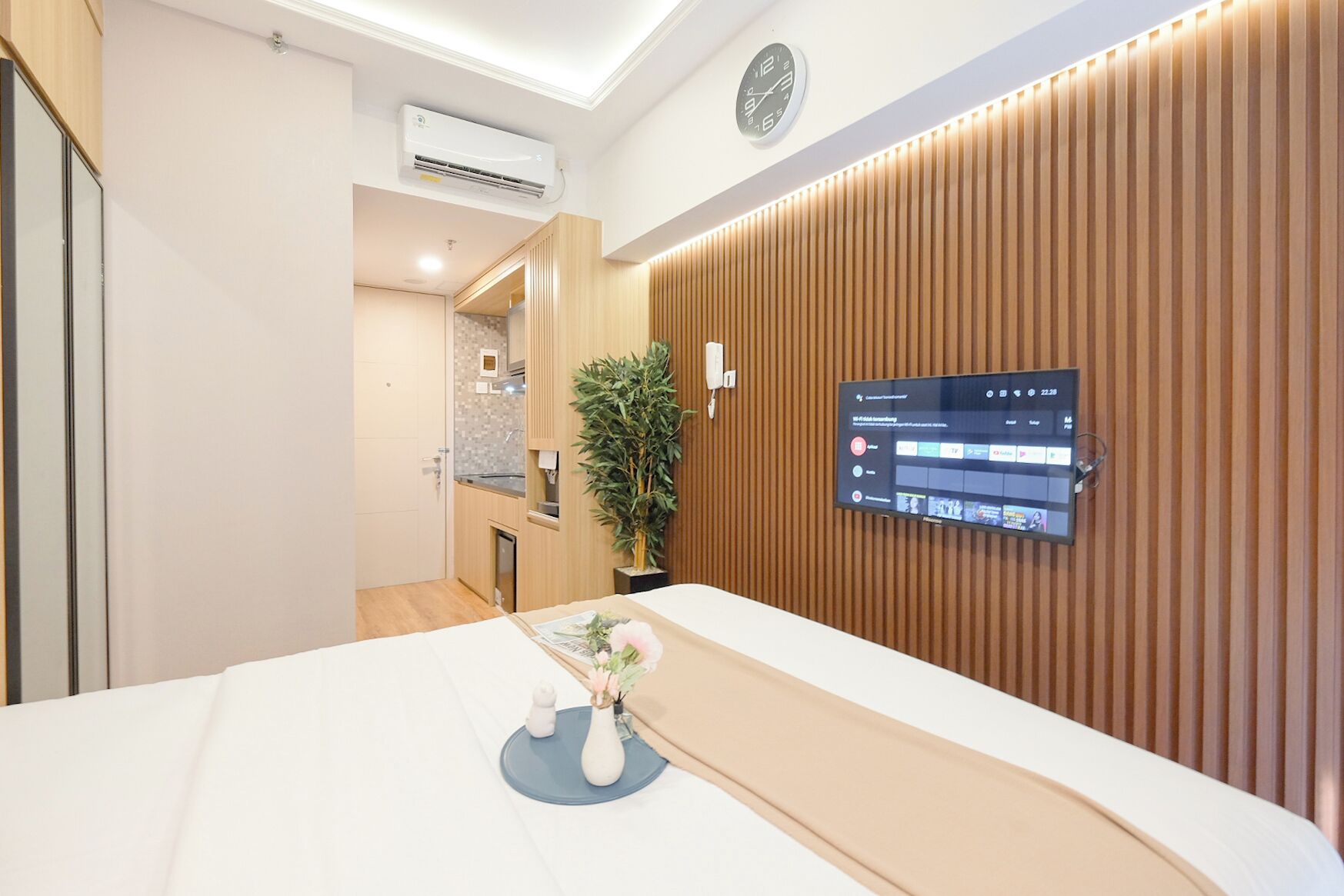 Habitación de hotel moderna con pared de paneles de madera, un televisor montado y una planta pequeña en la mesita de noche.