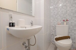 A bathroom with a white sink, toilet, and shower. There are toiletries on the sink and a towel on the toilet.