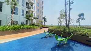 Un espace piscine sur le toit, avec un sol bleu, des chaises vertes et une vue sur un immeuble de grande hauteur doté de balcons.