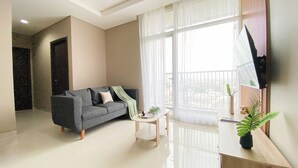 A modern living room with a grey sofa, a small white table, and a large window with sheer curtains.