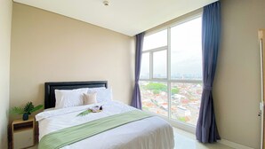 A hotel room with a large window, a bed with white linens, a green throw blanket, and a small plant on the nightstand.