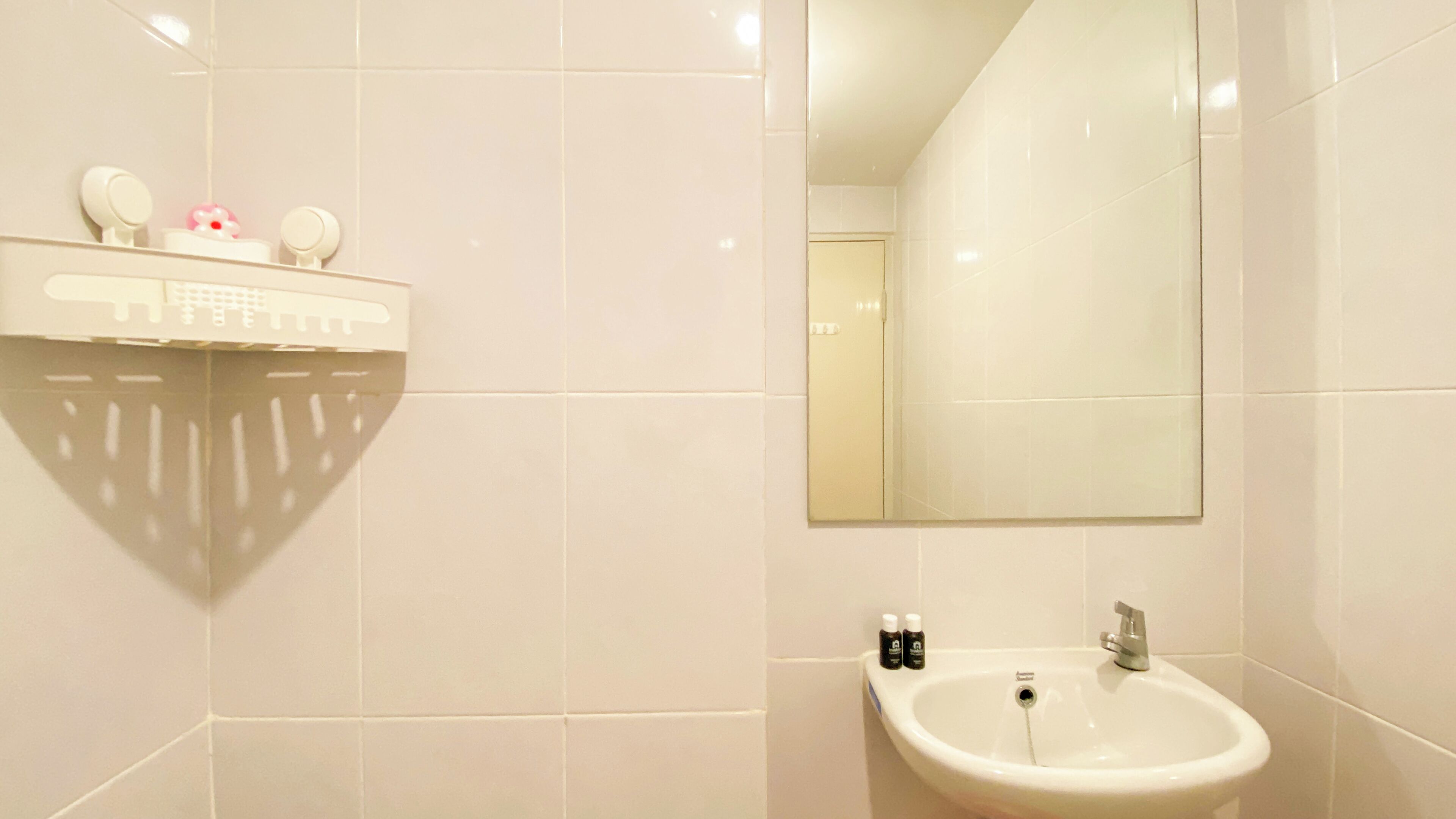 A bathroom with white tiles, a sink, a mirror, and a shelf with toiletries.