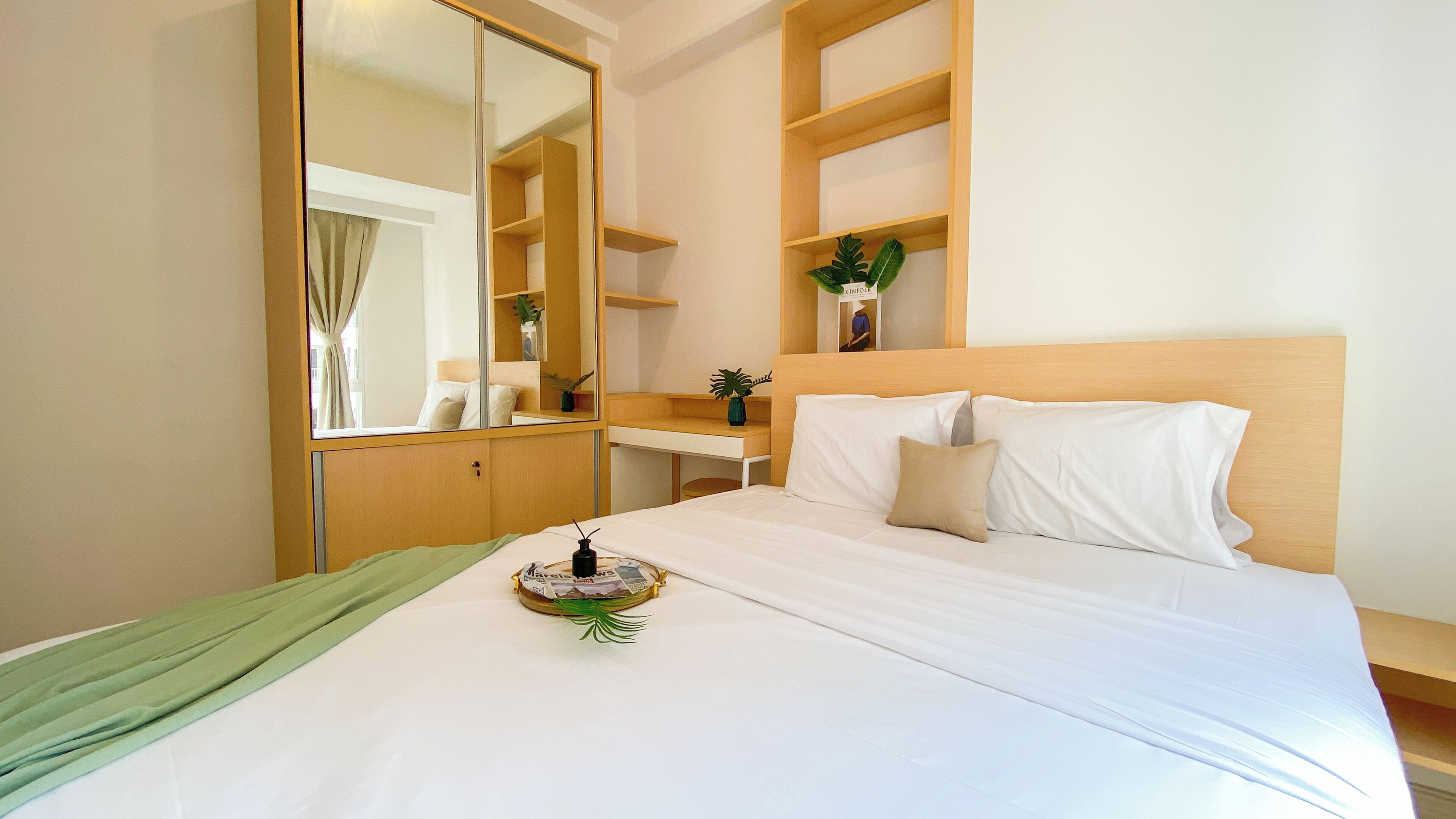 A hotel room with a bed, a bedside table, a mirror, a wardrobe, and a shelf with plants.