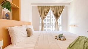 A hotel room with a bed, a nightstand, a window with curtains, and a plant on the windowsill. - Comfortable And Simply 2Br At Tokyo Riverside Pik 2 Apartment (Teluknaga)