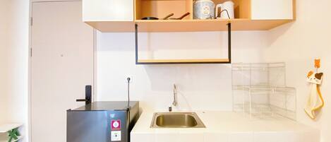 A compact kitchen with a refrigerator, a sink, and a countertop with a kettle and a coffee maker.