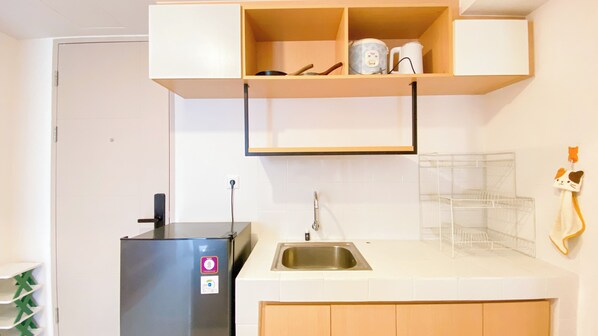 A compact kitchen with a refrigerator, a sink, and a countertop with a kettle and a coffee maker. - Comfortable And Simply 2Br At Tokyo Riverside Pik 2 Apartment (Teluknaga)