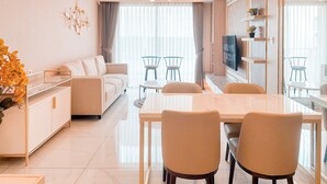 Ein modernes Wohnzimmer mit einer Couch, einem Esstisch und Stühlen. Ein Fernseher ist an der Wand montiert und auf dem Beistelltisch steht eine Pflanze.