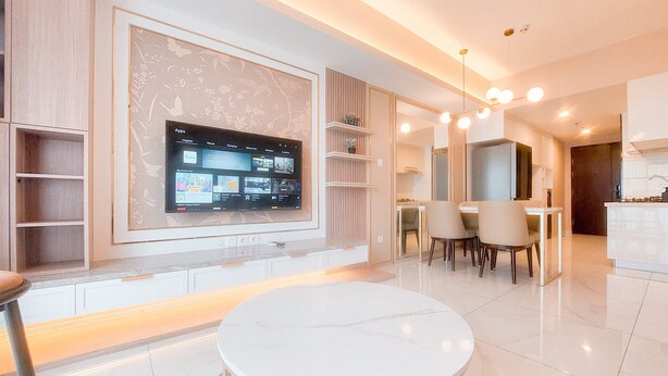 Ein modernes Wohnzimmer mit einem an der Wand montierten Flachbildfernseher, einem runden Esstisch und einer Küche im Hintergrund.