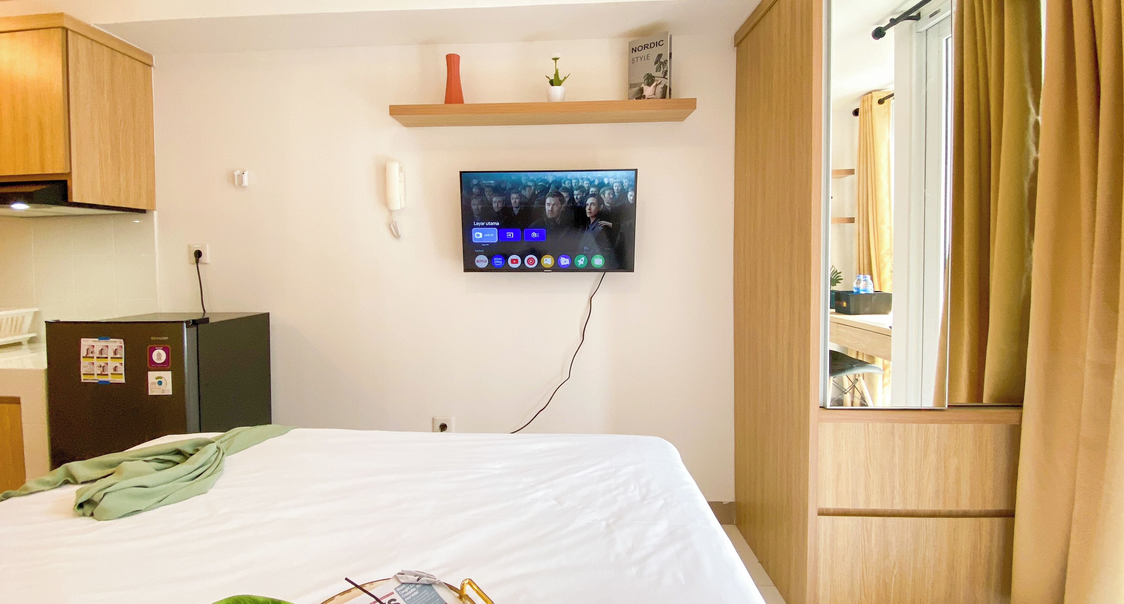 A hotel room with a bed, a TV mounted on the wall, a small desk, and a wardrobe.