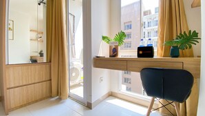 Una habitación de hotel moderna con un ventanal grande, un escritorio de madera, una silla y una pequeña planta sobre el escritorio.
