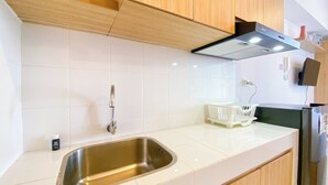 A modern kitchen with white tiles, stainless steel sink, wooden cabinets, and a black range hood. - Modern And Tranquil Studio At Apartment Tokyo Riverside Pik 2 (Teluknaga)