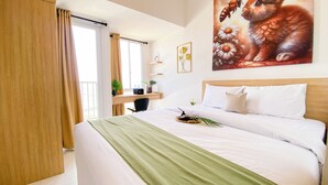 A hotel room with a large bed, a desk with a chair, a window with curtains, and a painting of a cat on the wall. - Modern And Tranquil Studio At Apartment Tokyo Riverside Pik 2 (Teluknaga)