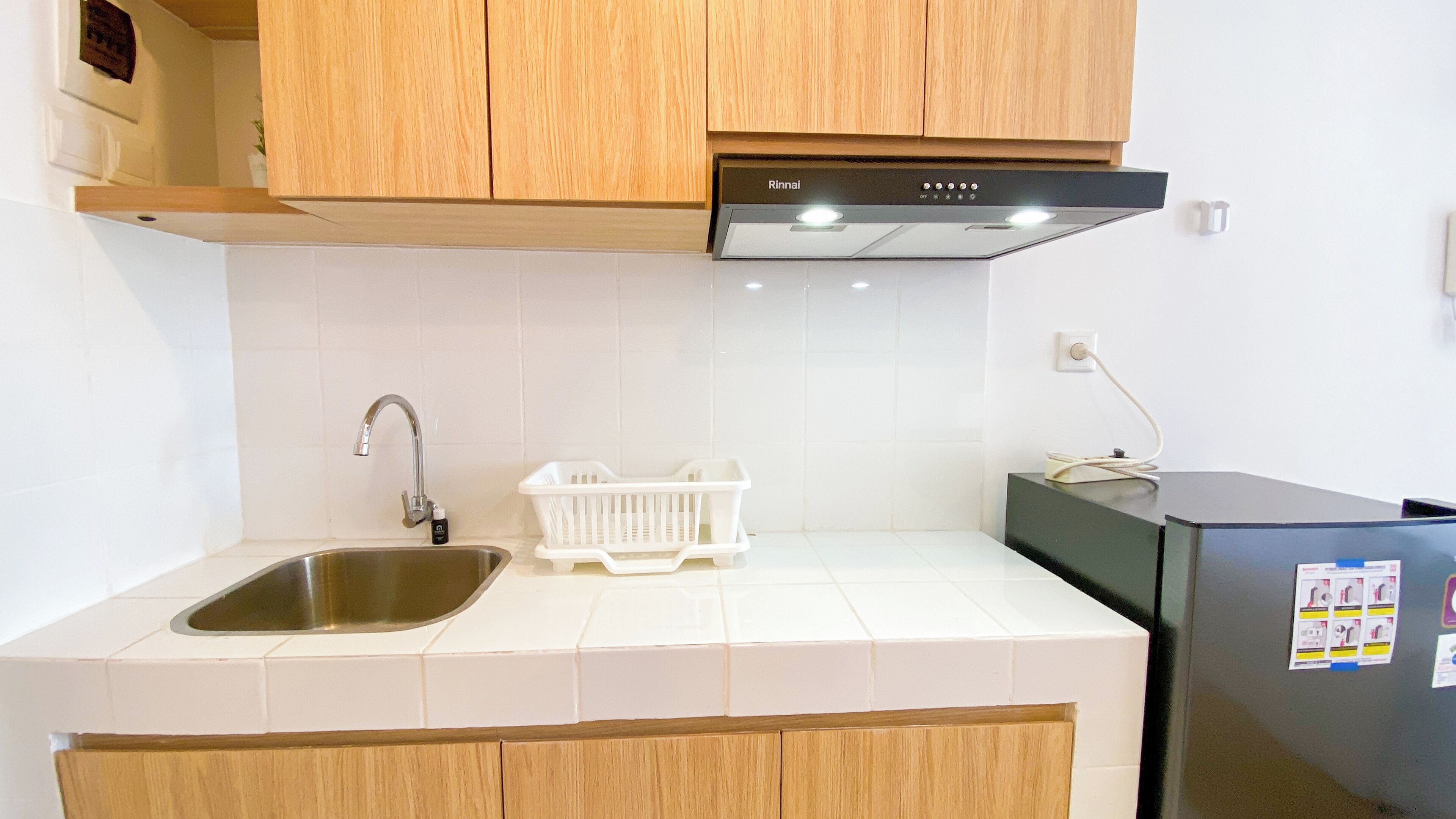 Una cucina con lavello in acciaio inossidabile, piano di lavoro bianco, mobili in legno e frigorifero nero.
