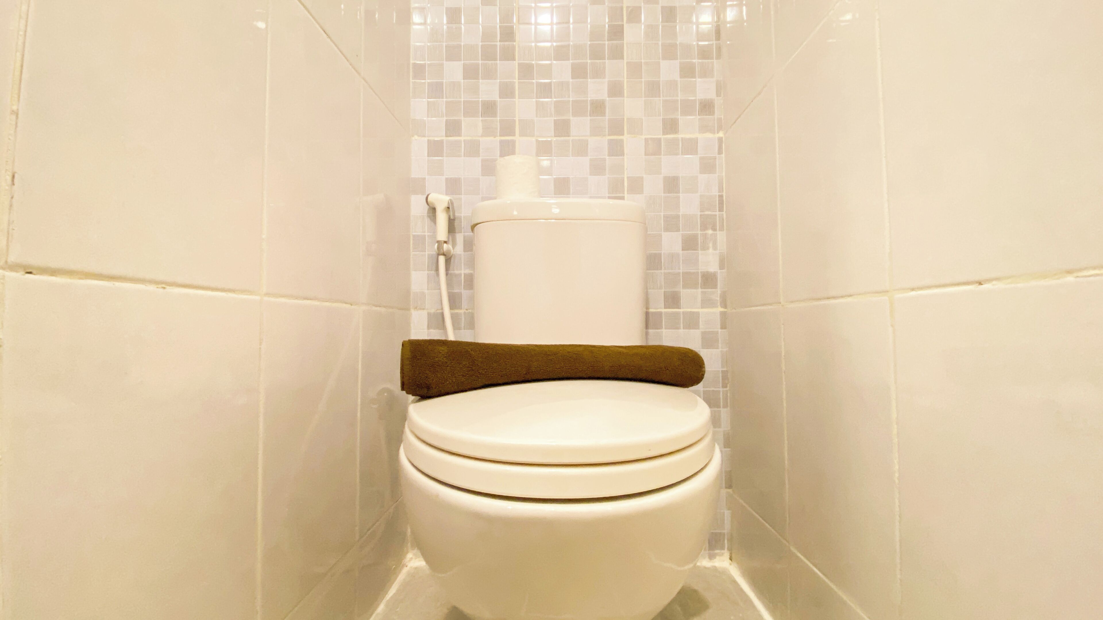 A white toilet with a brown seat cover in a bathroom with white tiled walls and floor.