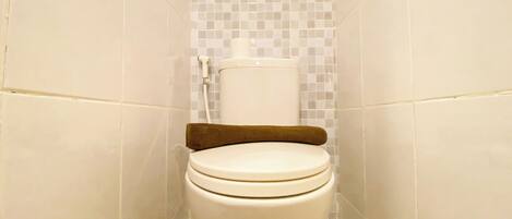 A white toilet with a brown seat cover in a bathroom with white tiled walls and floor.