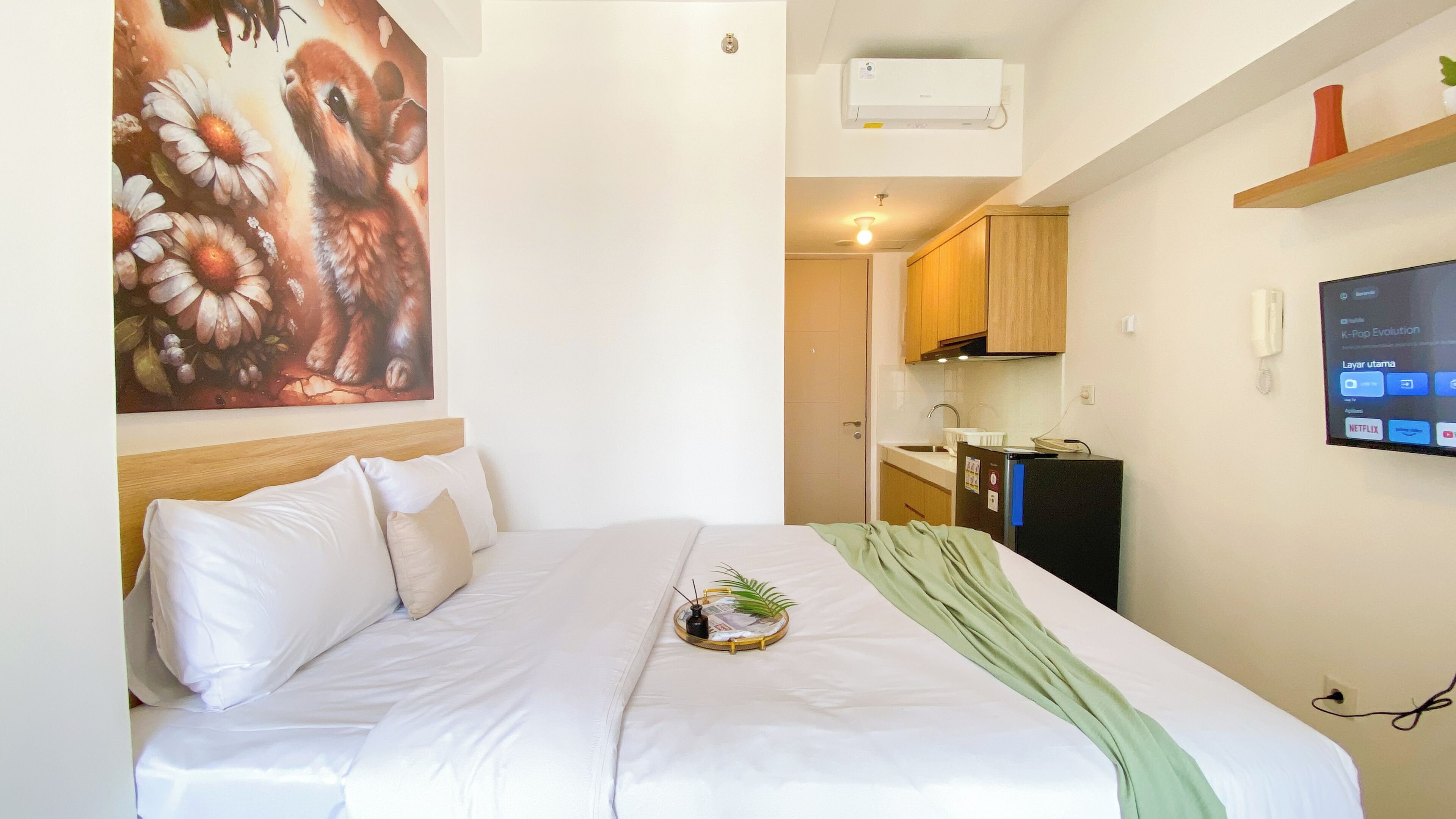 Une chambre d’hôtel équipée d’un lit, d’un tableau, d’une télévision, d’un coin cuisine et d’un téléphone fixé au mur.