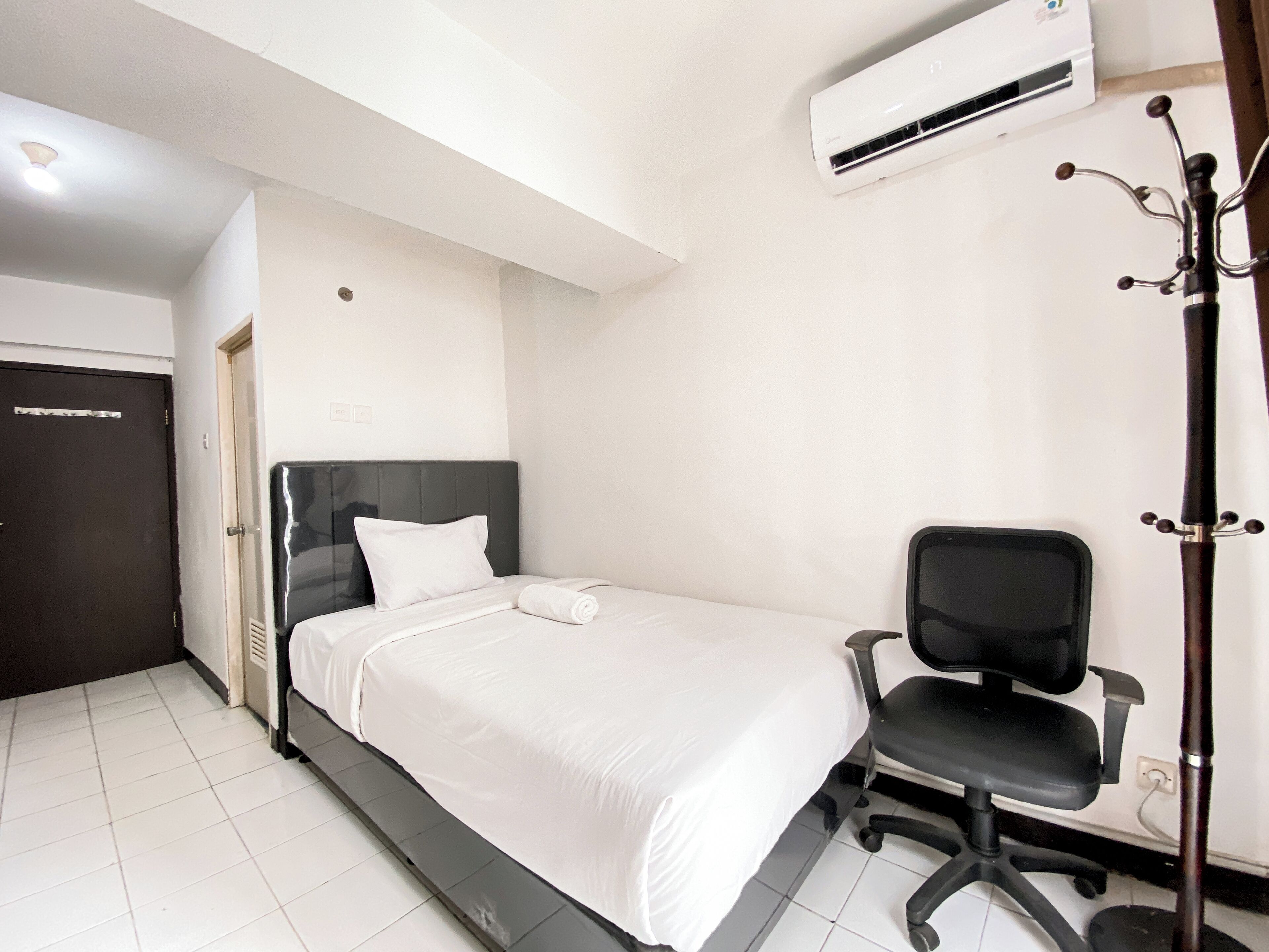 A hotel room with a bed, a chair, an air conditioning unit, and a door.