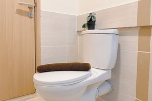 Eine Toilette mit einem braunen Handtuch auf dem Sitz, einem kleinen Topfpflanz auf dem Tank und beige gefliesten Wänden.