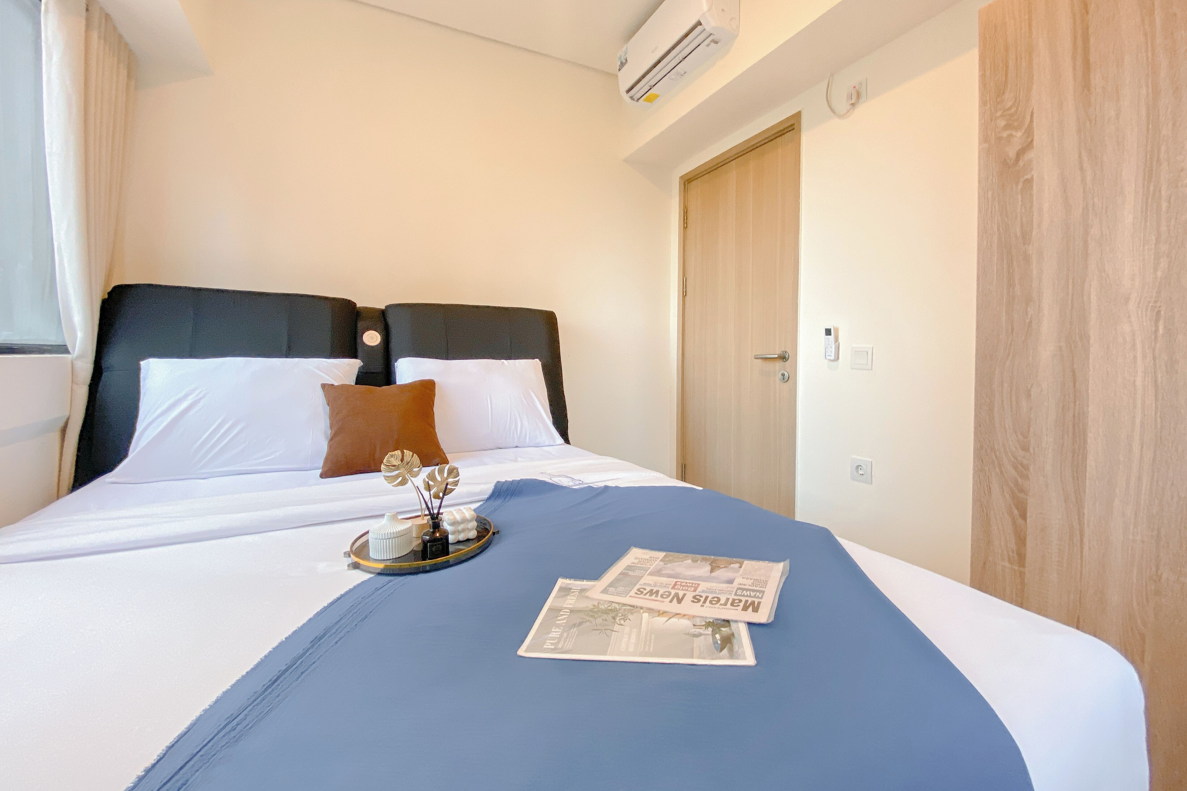 A hotel room with a bed, a wooden door, and an air conditioning unit.