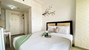 A hotel room with a bed, a nightstand, a wall-mounted decoration, and a door. - Homey And Cozy Living Studio At Poris 88 Apartment (Tangerang)