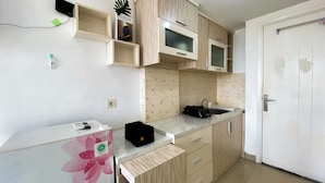 A kitchen with wooden cabinets, a microwave, a sink, and a refrigerator. - Homey And Cozy Living Studio At Poris 88 Apartment (Tangerang)
