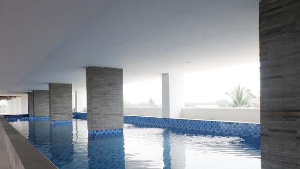 An indoor swimming pool with clear blue water, supported by stone pillars, and large windows allowing natural light. - Homey And Cozy Living Studio At Poris 88 Apartment (Tangerang)