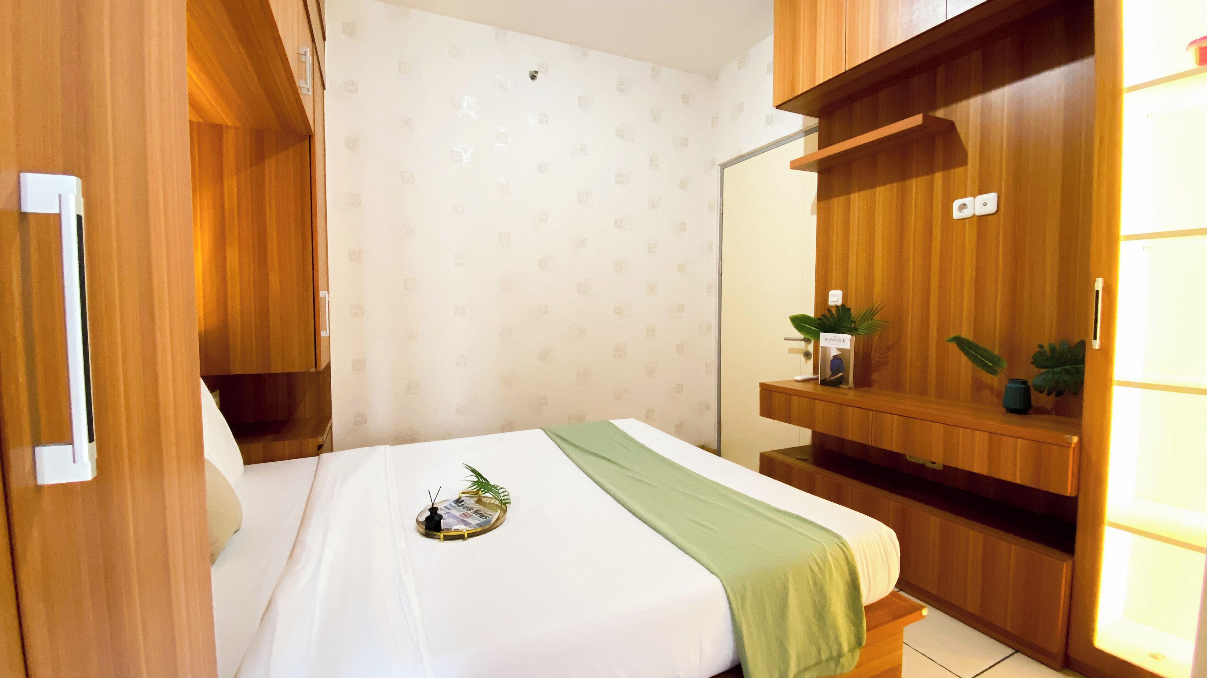 A hotel room with a bed, wooden wardrobe, and a small shelf with a plant.