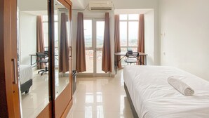 Ein Hotelzimmer mit Bett, Schreibtisch, Stuhl, Spiegel und Blick auf die Stadt durch das Fenster.