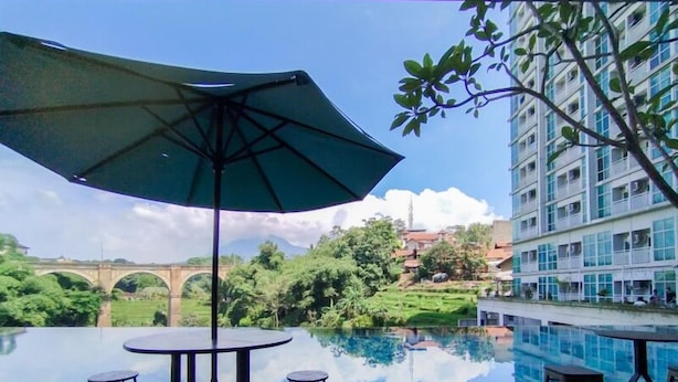Ein Pool ohne Ende mit Blick auf eine Brücke und Grünflächen, einem Tisch und Stühlen sowie einem großen Sonnenschirm.
