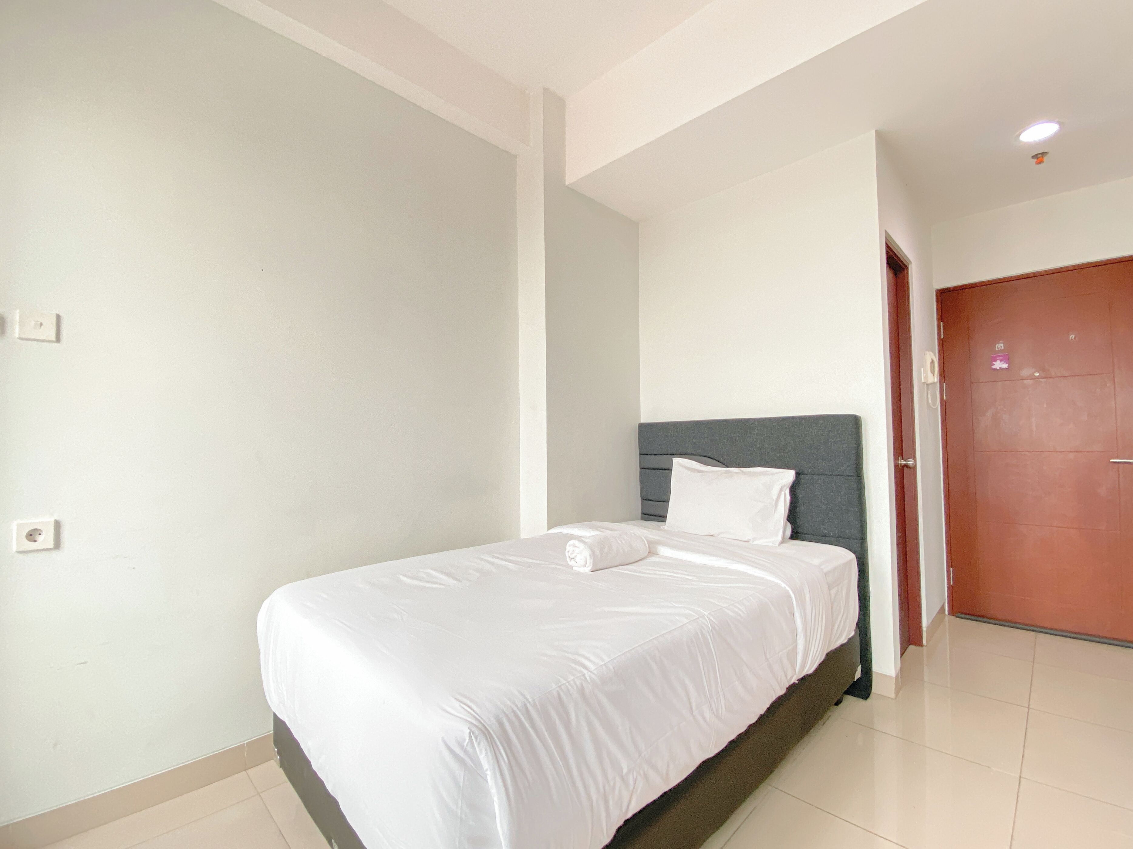 A bedroom with a bed, a grey headboard, white walls, and a wooden door.
