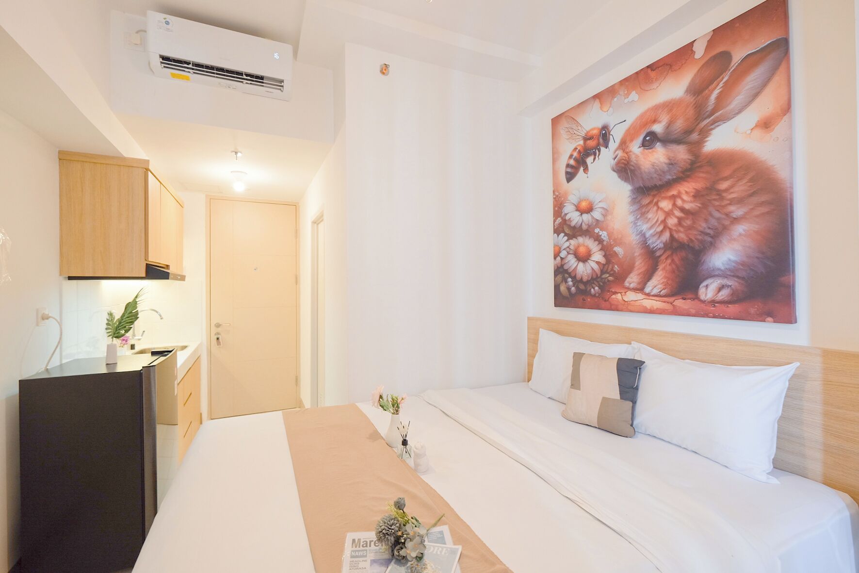 Ein Schlafzimmer mit Bett, einem Hasenbild, einem kleinen Tisch und einer Küchenzeile.