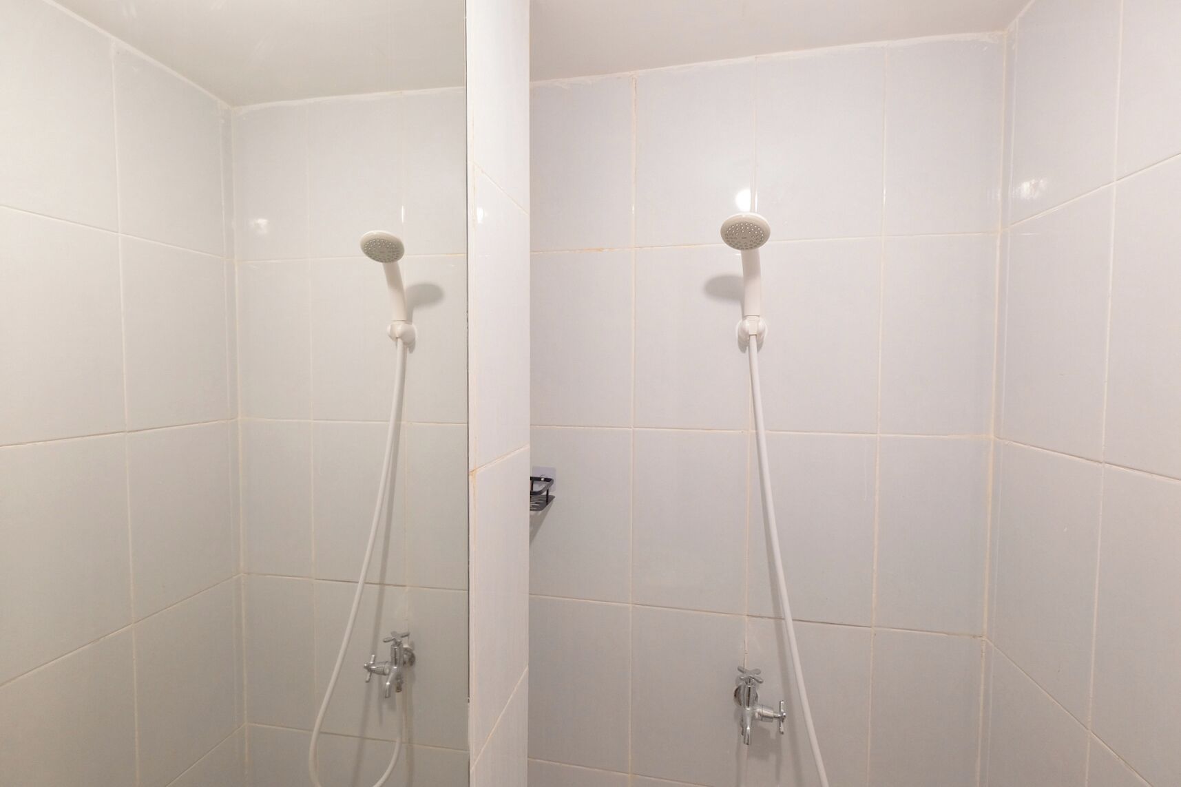 A shower area with white tiled walls and two showerheads.