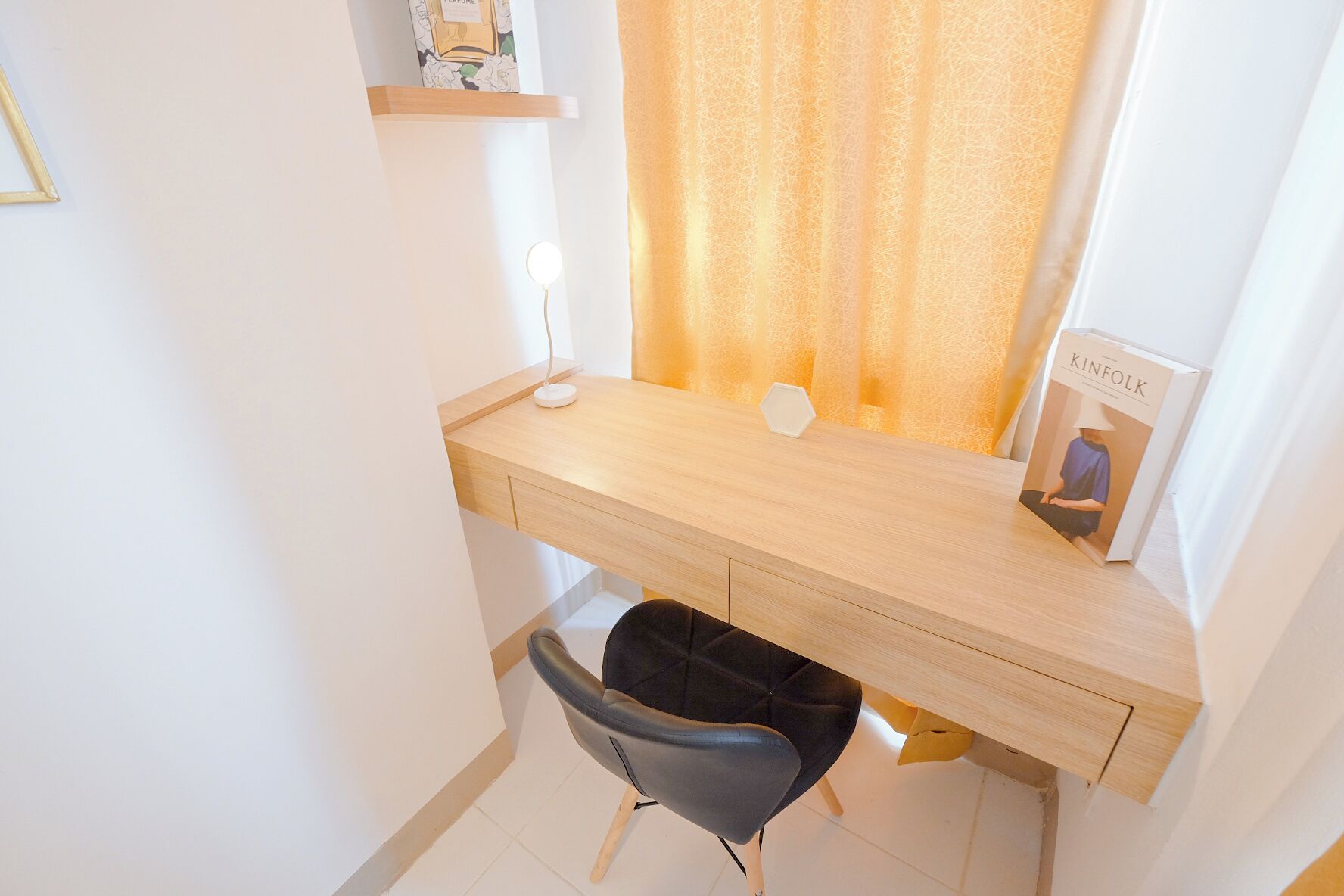 A compact workspace with a wooden desk, a black chair, a small waste bin, and a book titled "KINFOLK" on the desk.
