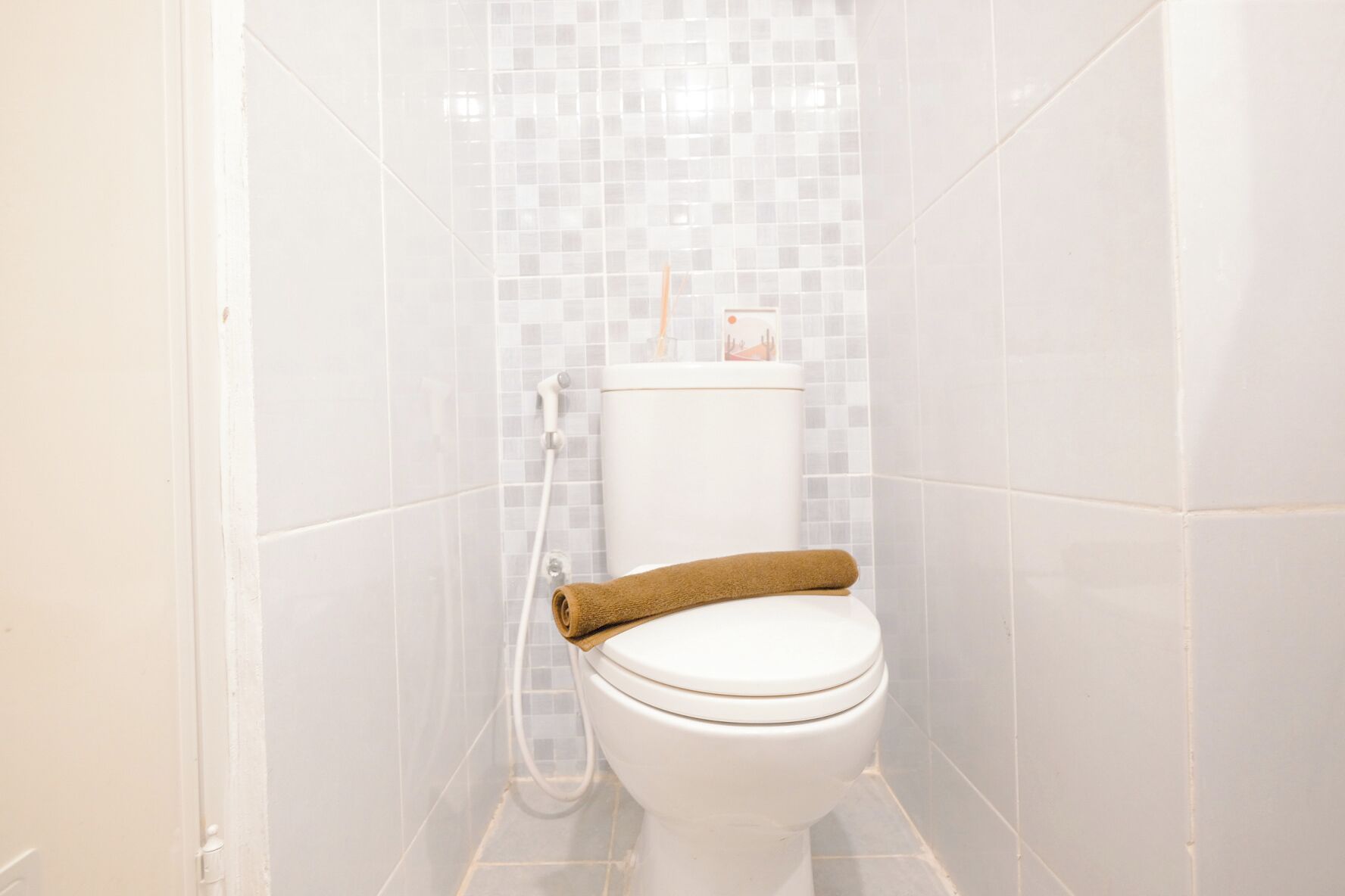 A bathroom with a white toilet, a towel on the seat, and a shower area with tiled walls.