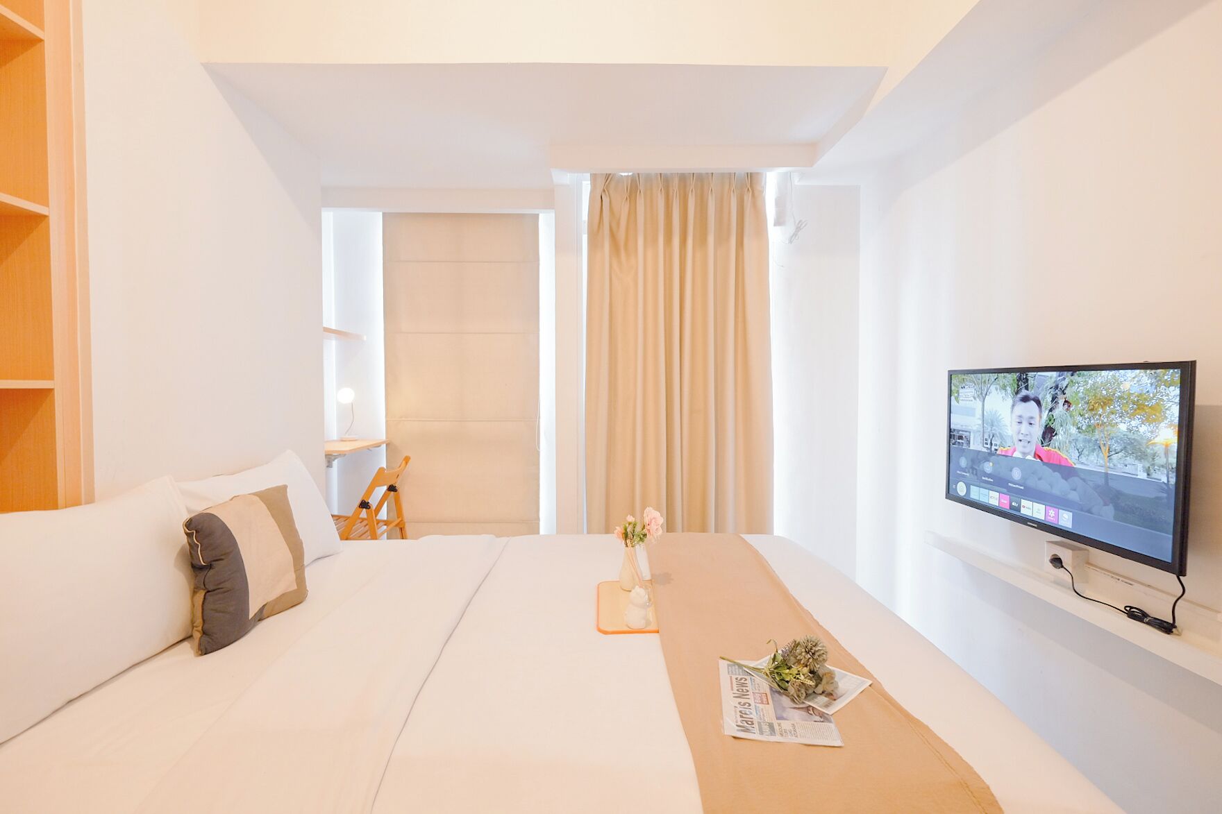 Ein modernes Hotelzimmer mit einem Bett, einem Holznachttisch, einem Fernseher und einem mit Vorhängen versehenen Fenster.