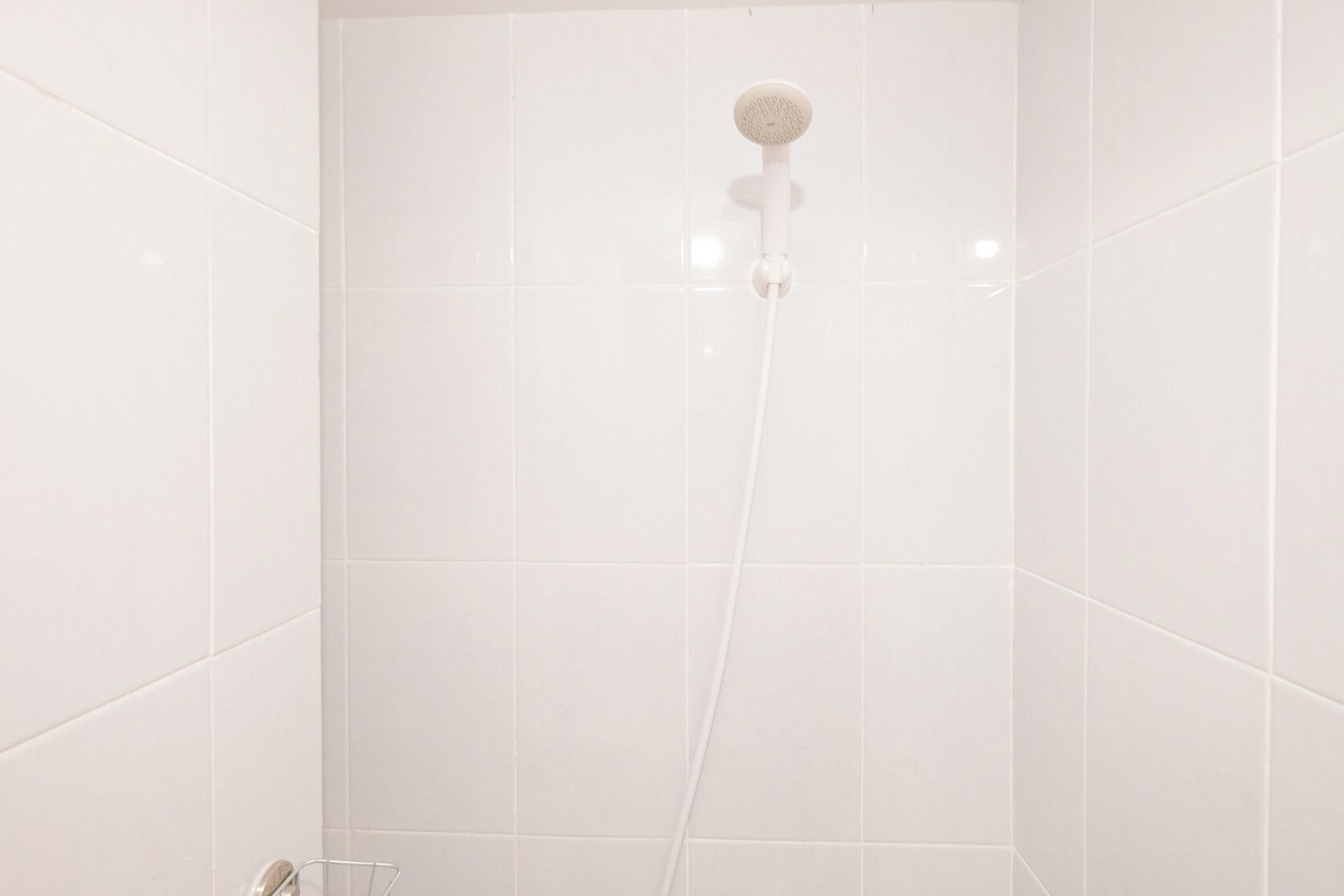 Een badkamer met witte tegels, een douchekop en een metalen rek.