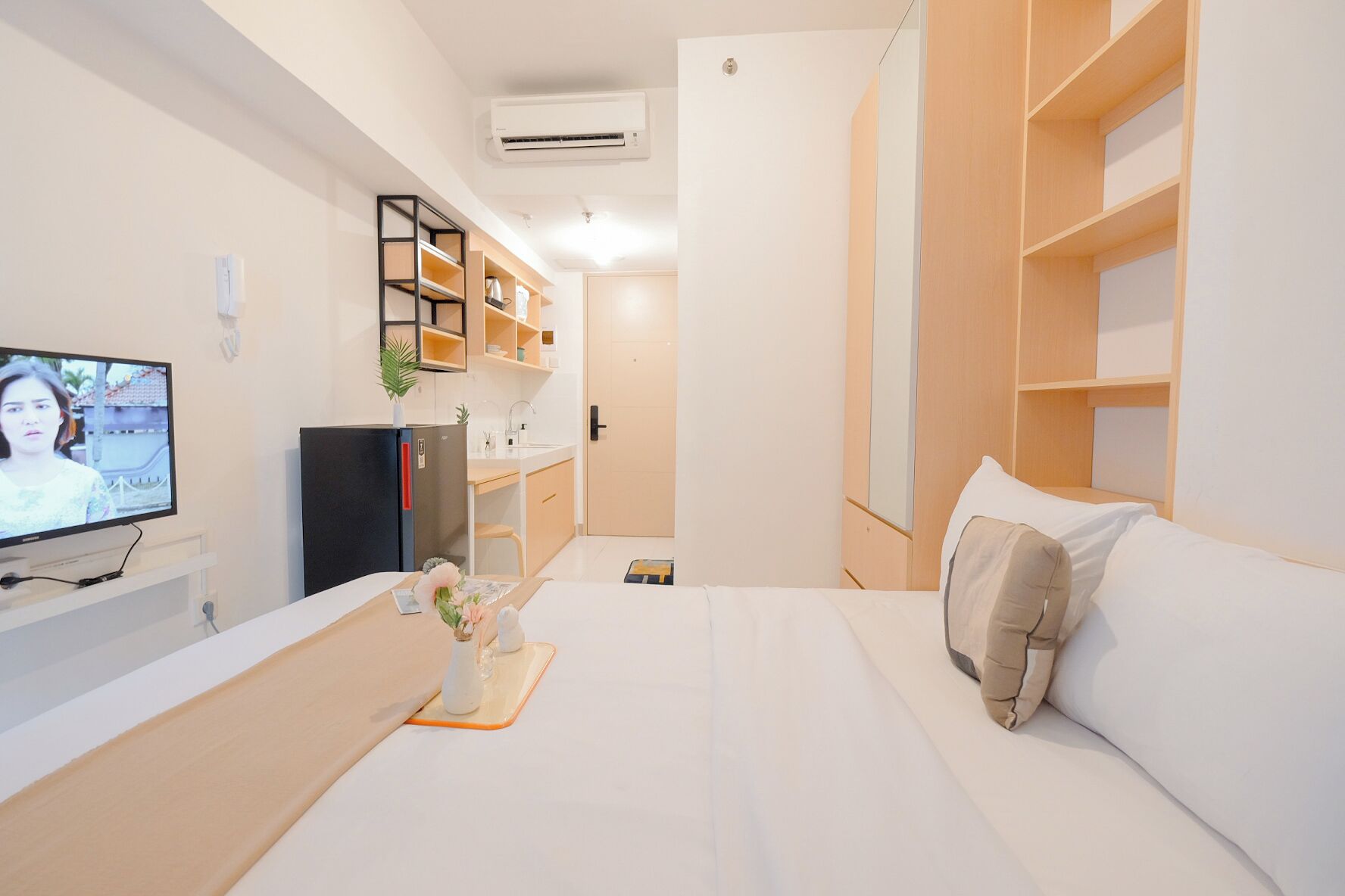 A modern hotel room with a bed, a TV, a kitchenette, and a wardrobe.